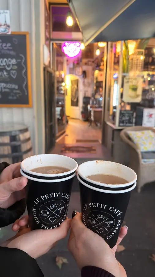 Zwei Kaffeebecher mit dem Le-Petit-Café-Logo vor dem Eingang des Cafés