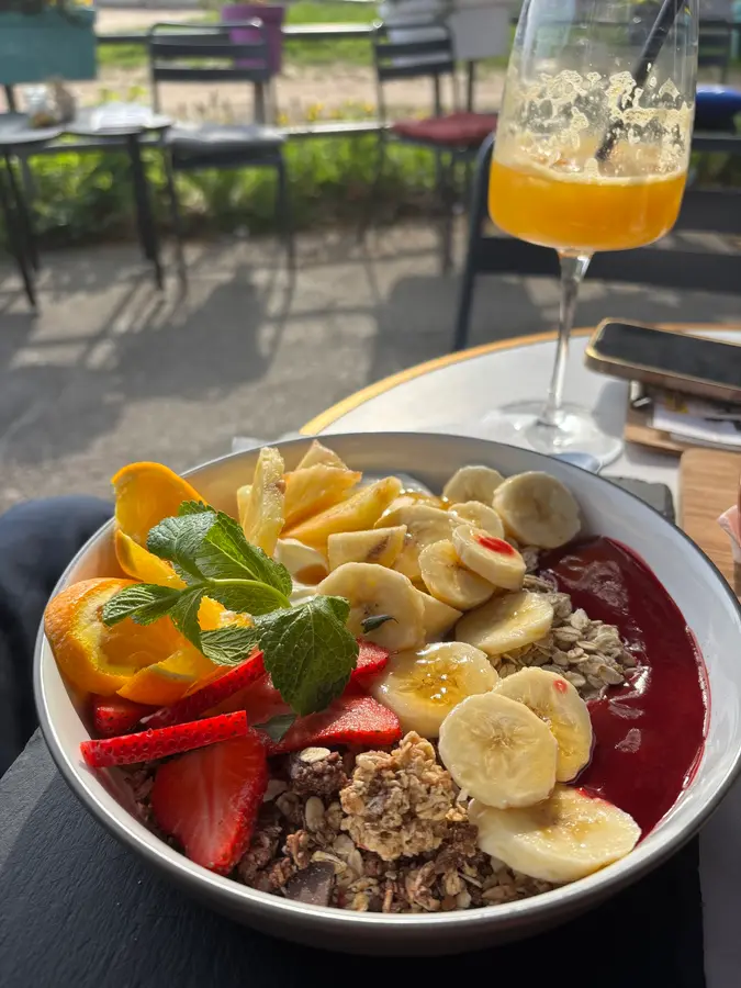 Bowl mit Banane, Erdbeeren, Mango, Granola und Beeren-Püree, dazu ein Orangensaft