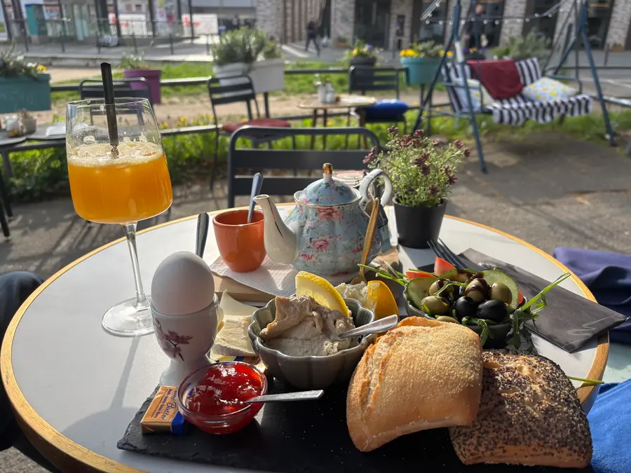 Frühstück in der Sonne am Danziger Platz: Orangensaft, Porzellan-Teekanne, Ei, Brötchen und Oliven