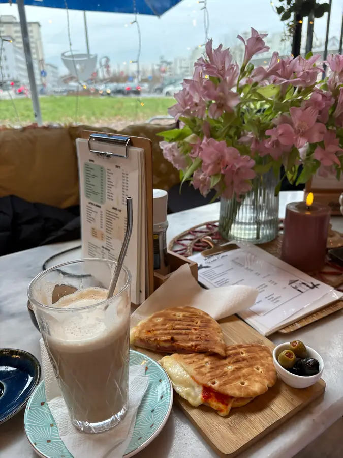 Eiskaffee, Panini und Oliven auf einem Tisch mit rosa Blumen