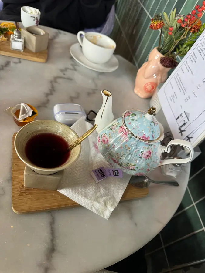 Geblümte Porzellan-Teekanne und eine Tasse Tee auf einem Marmortisch vor grünen Fliesen